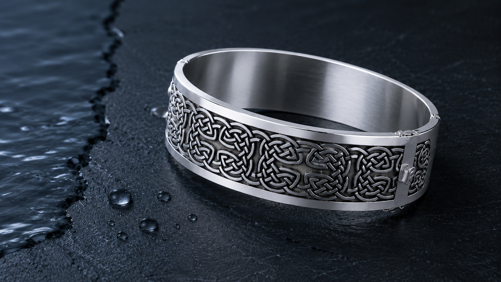 Wide sterling silver Celtic knotwork hinged bangle bracelet beside water droplets on dark slate.