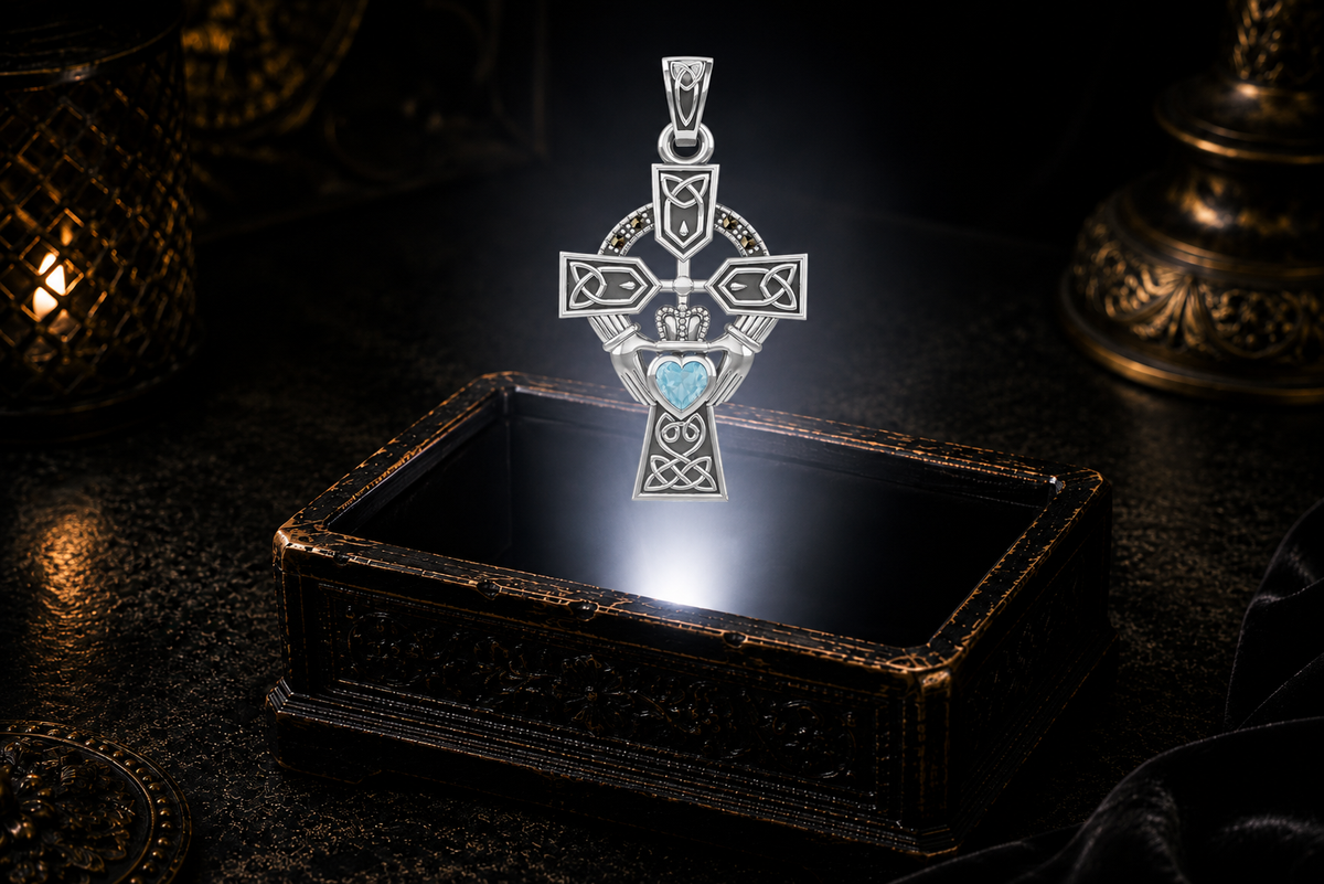 14K white gold Celtic Cross pendant featuring a blue topaz Claddagh heart and marcasite halo, hovering over an ornate keepsake box.