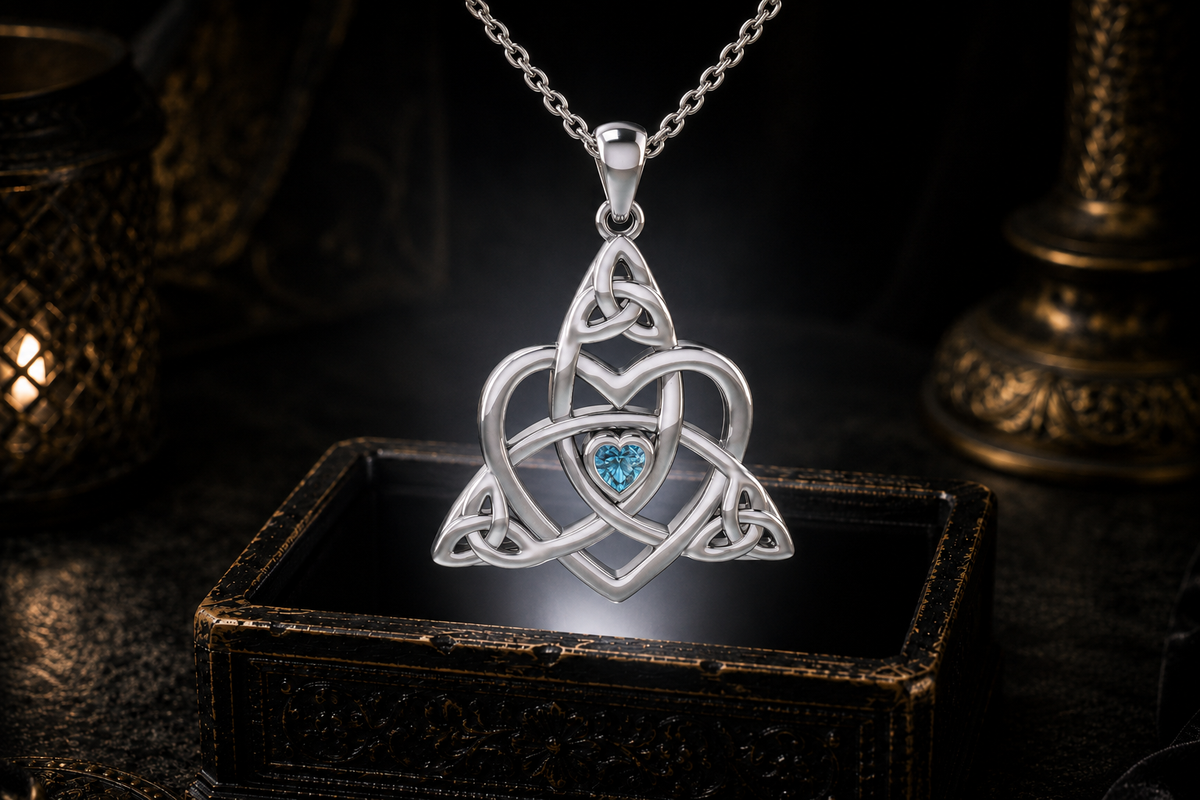 Blue topaz Celtic heart pendant with Trinity knotwork and silver cable chain suspended above an antique jewelry box with warm ambient lighting