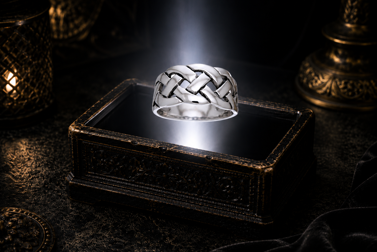 Braided .925 sterling silver Celtic knot ring suspended above an ornate antique jewelry box within a neutral white beam of light in a dark luxury setting.