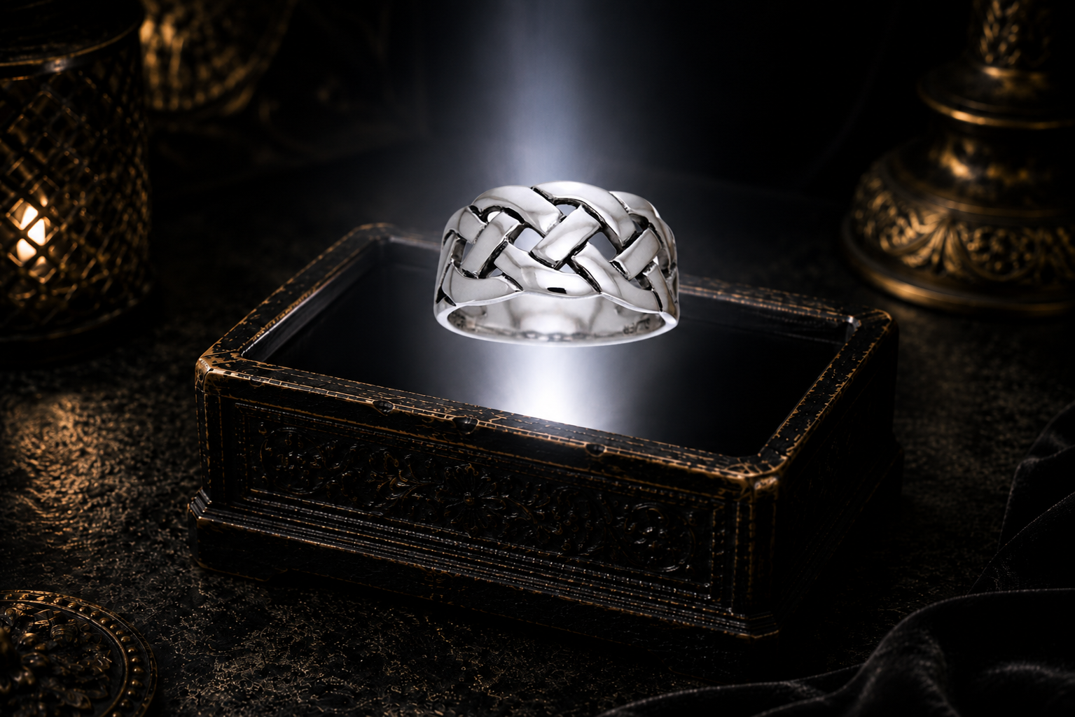 Braided .925 sterling silver Celtic knot ring suspended above an ornate antique jewelry box within a neutral white beam of light in a dark luxury setting.