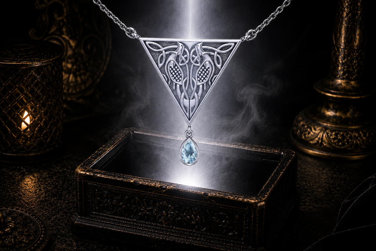 Sterling silver Celtic bird knotwork necklace with blue topaz gemstone displayed above a luminous jewelry chest in a cinematic shadowed environment with elegant reflections.