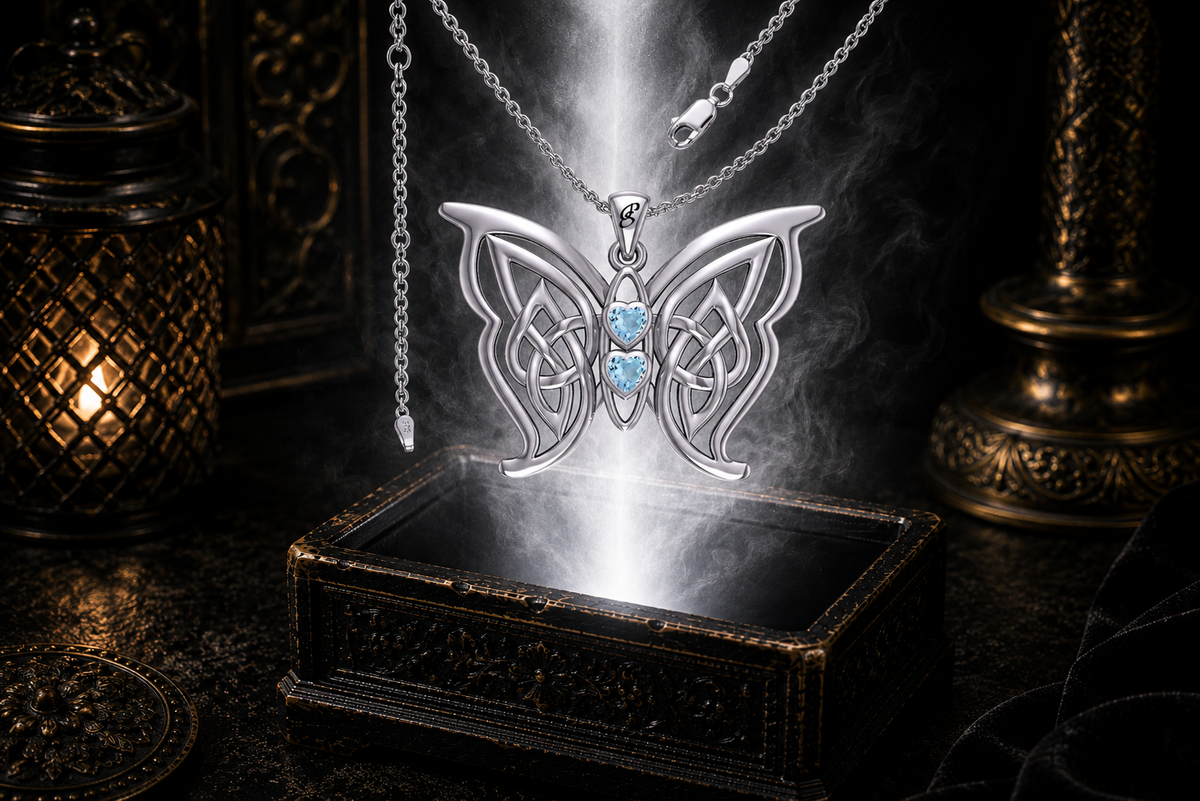 Sterling silver Celtic butterfly pendant with twin blue topaz heart gemstones floating above an ornate dark jewelry box surrounded by luminous white light and drifting mist in a cinematic luxury setting.
