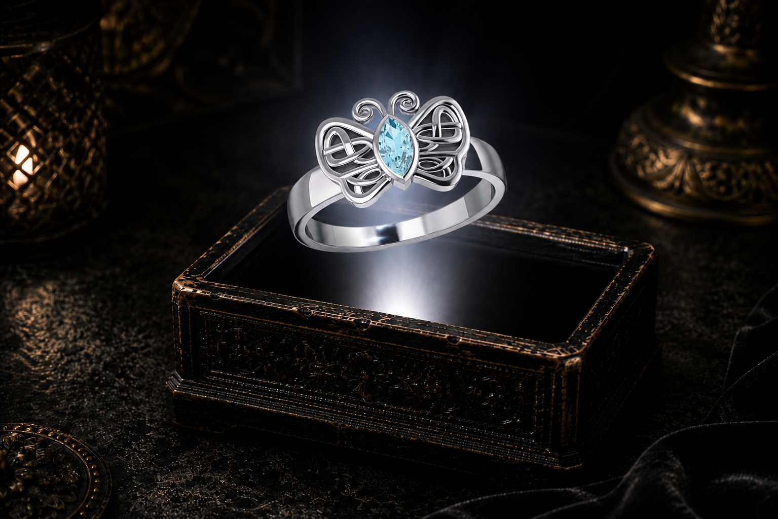 Celtic butterfly ring in sterling silver featuring a marquise-cut blue topaz gemstone hovering over an ornate keepsake box illuminated by warm candlelight.