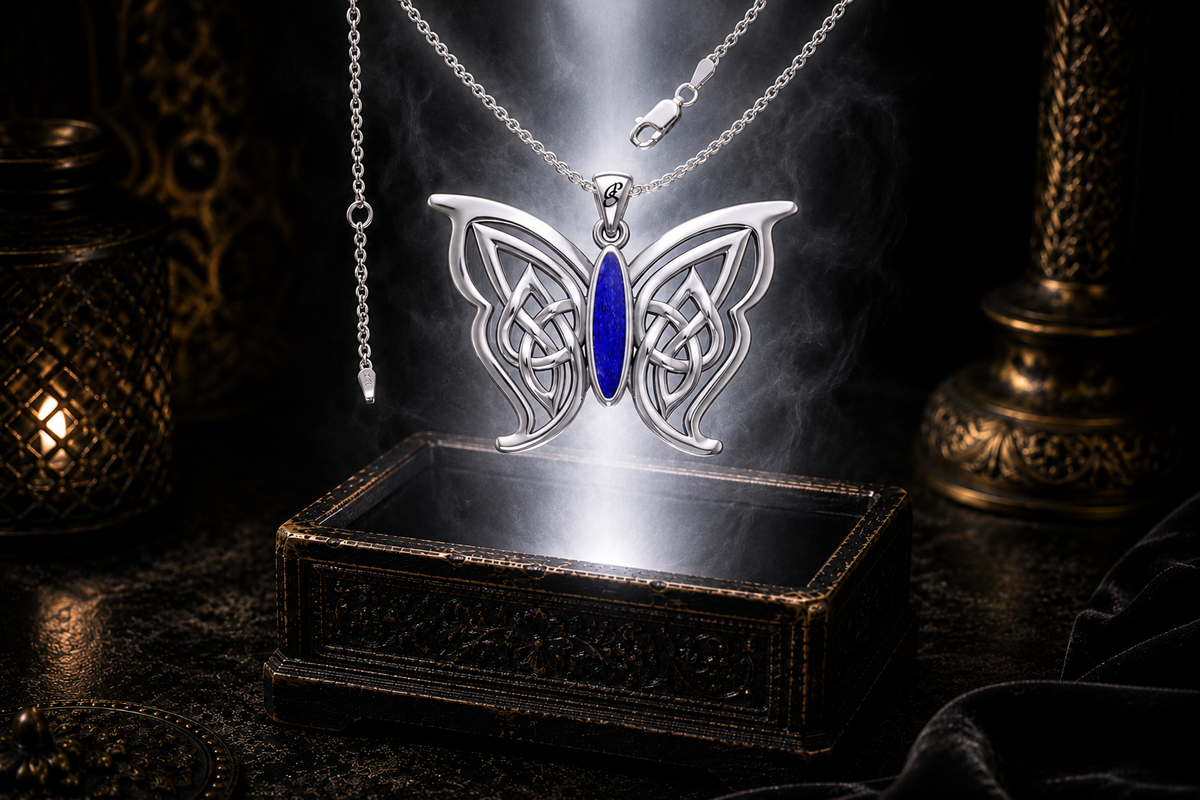 Sterling silver Celtic butterfly pendant with chain and lapis gemstone inlay floating above an ornate dark jewelry box surrounded by luminous white light in a cinematic luxury setting.
