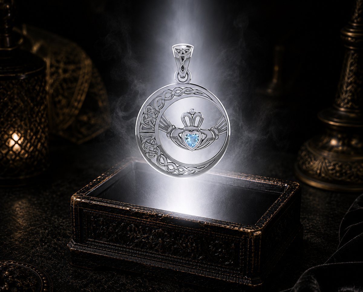 Sterling silver Irish Claddagh Moon pendant with blue topaz heart gemstone displayed above a luminous jewelry chest in a cinematic shadowed setting, showcasing a crescent moon, Celtic knotwork, and traditional Claddagh symbolism.