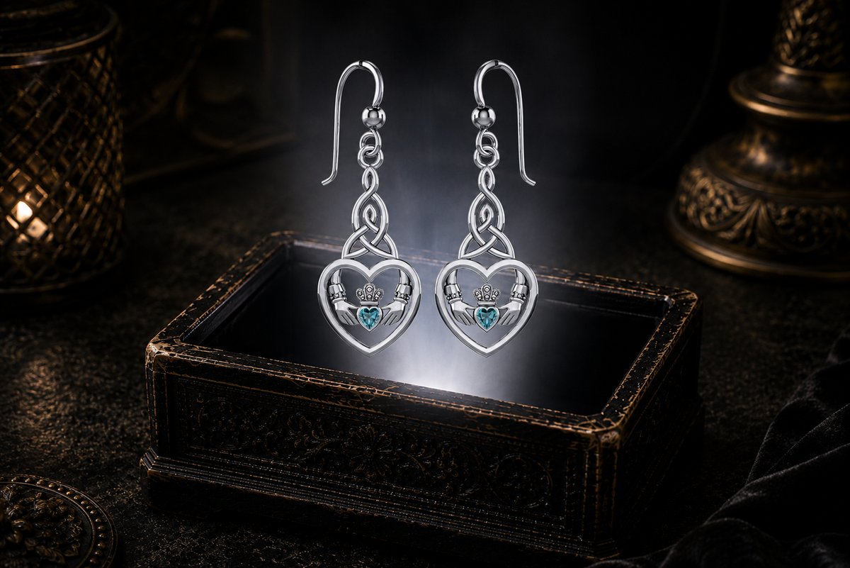 Sterling silver Celtic Claddagh Trinity knot heart earrings with blue topaz gemstones floating above a glowing ornate jewelry box in a dark luxury setting