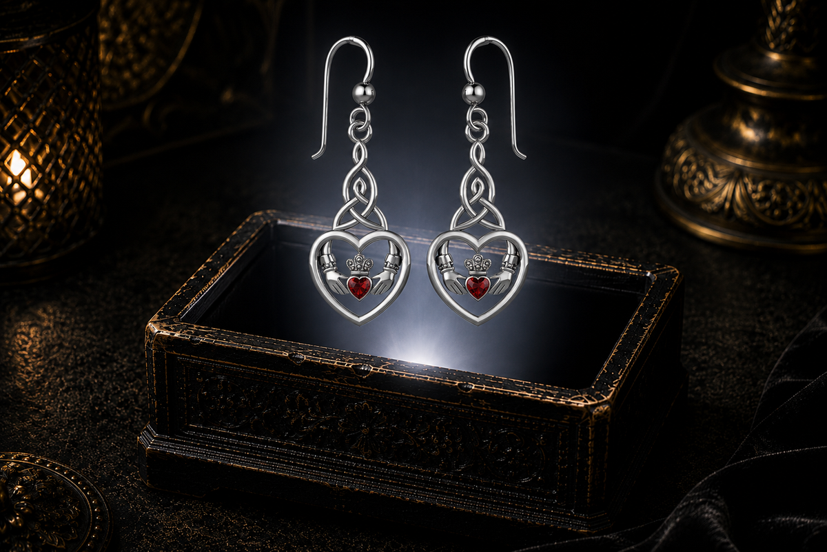 Sterling silver Celtic Claddagh Trinity knot heart earrings with garnet gemstones floating above a glowing ornate jewelry box in a dark luxury setting