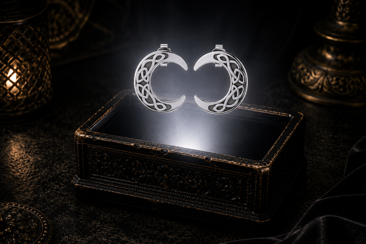 Sterling silver Celtic crescent moon stud earrings with Trinity knotwork floating above a glowing ornate jewelry box in a dark luxury setting