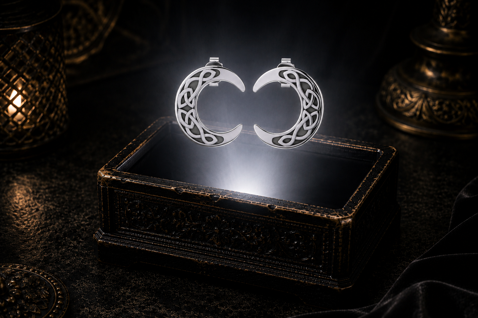 Sterling silver Celtic crescent moon stud earrings with Trinity knotwork floating above a glowing ornate jewelry box in a dark luxury setting