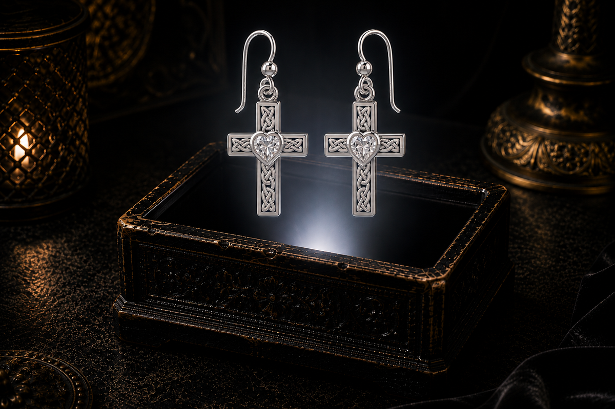 Sterling silver Celtic cross earrings with cubic zirconia heart gemstones floating above a glowing ornate jewelry box in a dark luxury setting