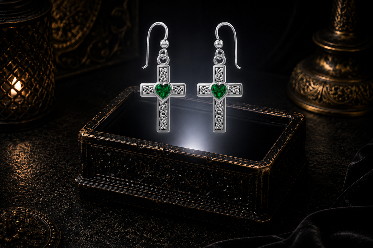 Sterling silver Celtic cross earrings with emerald glass heart gemstones floating above a glowing ornate jewelry box in a dark luxury setting