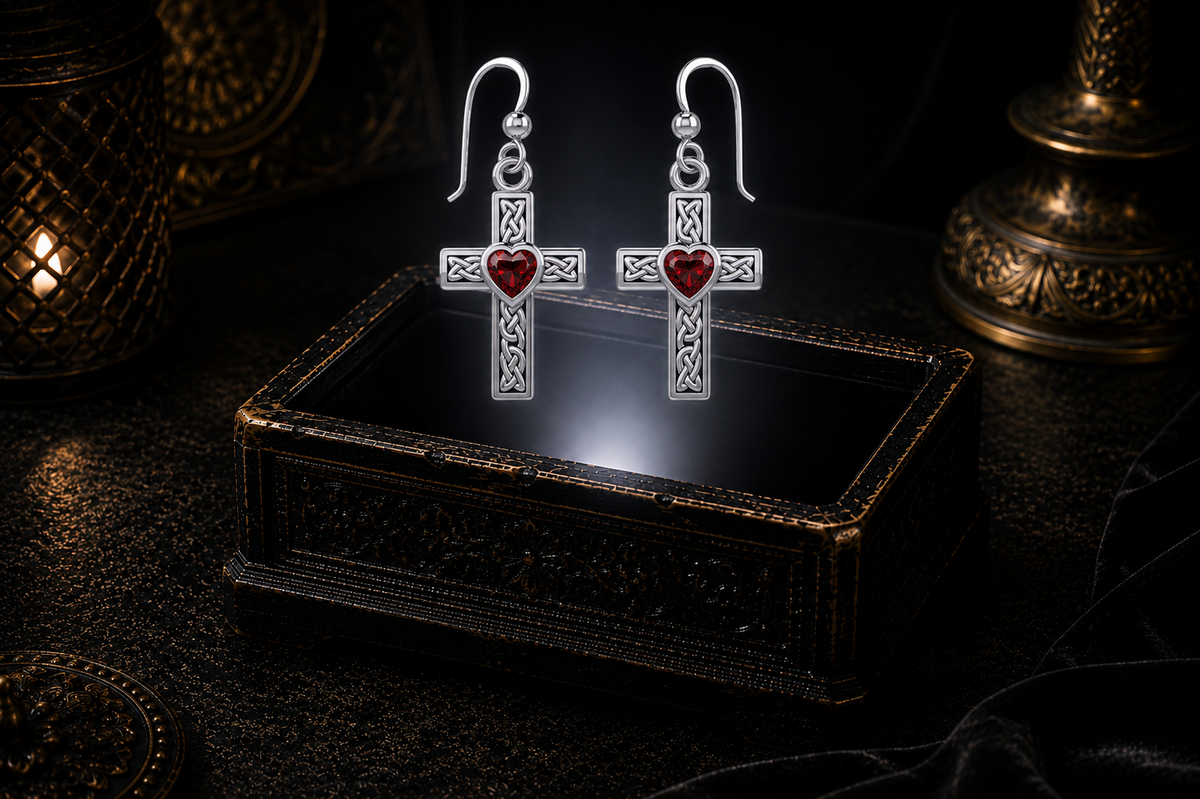 Sterling silver Celtic cross earrings with garnet heart gemstones floating above a glowing ornate jewelry box in a dark luxury setting