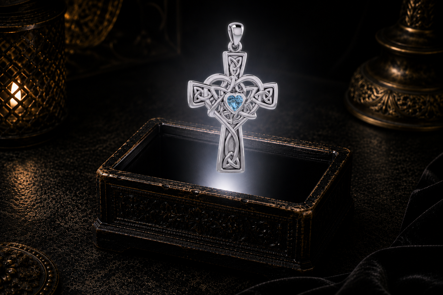 Sterling silver Celtic Heart Cross pendant with a heart-shaped Blue Topaz gemstone suspended above an antique jewelry box illuminated by warm candlelight.