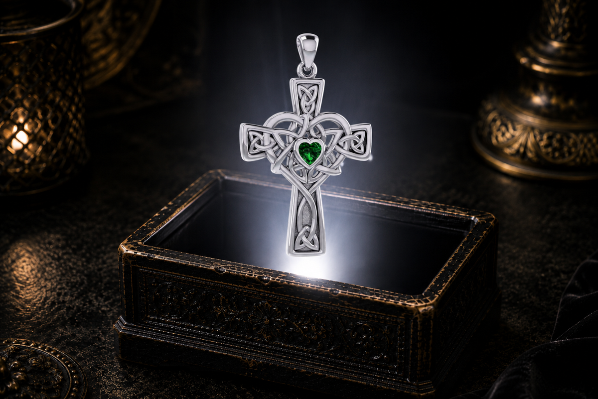 Sterling silver Celtic Heart Cross pendant featuring a heart-shaped Emerald Glass gemstone floating above an antique jewelry box in a refined dark setting.