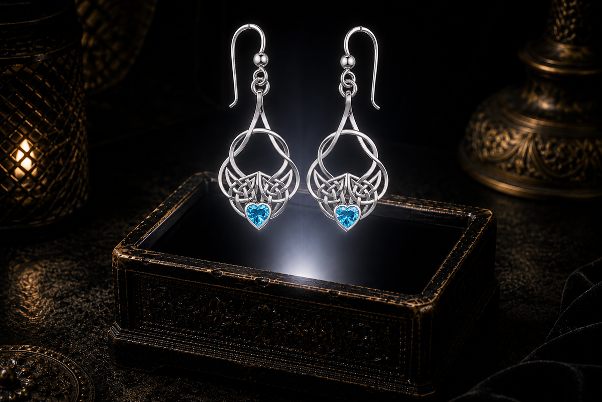 Sterling silver Celtic heart knot earrings with blue topaz heart gemstones floating above a glowing ornate jewelry box in a dark luxurious mystical setting