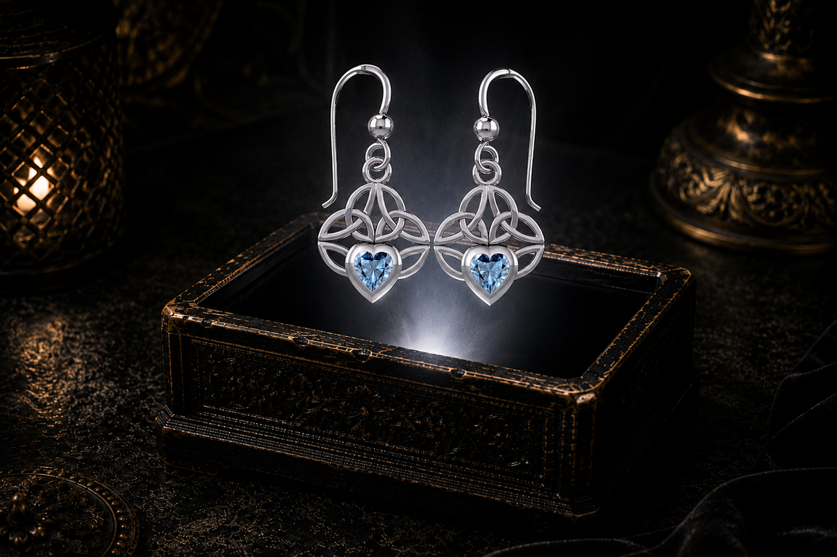 Sterling silver Celtic knot earrings with blue topaz heart gemstones floating above a glowing ornate jewelry box in a dark luxury setting