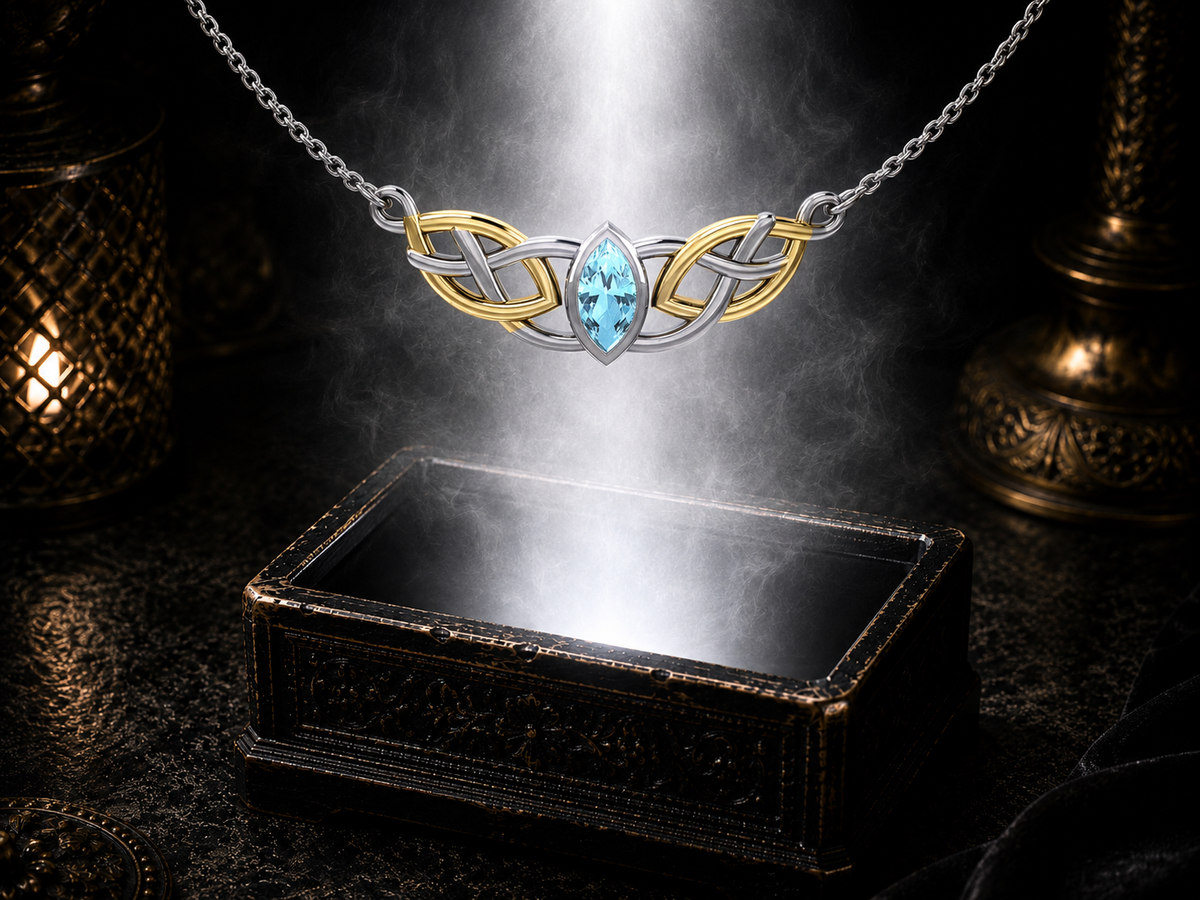 Sterling silver Celtic knotwork necklace with 14K gold accents and blue topaz gemstone displayed above a luminous jewelry chest within a cinematic shadowed setting.
