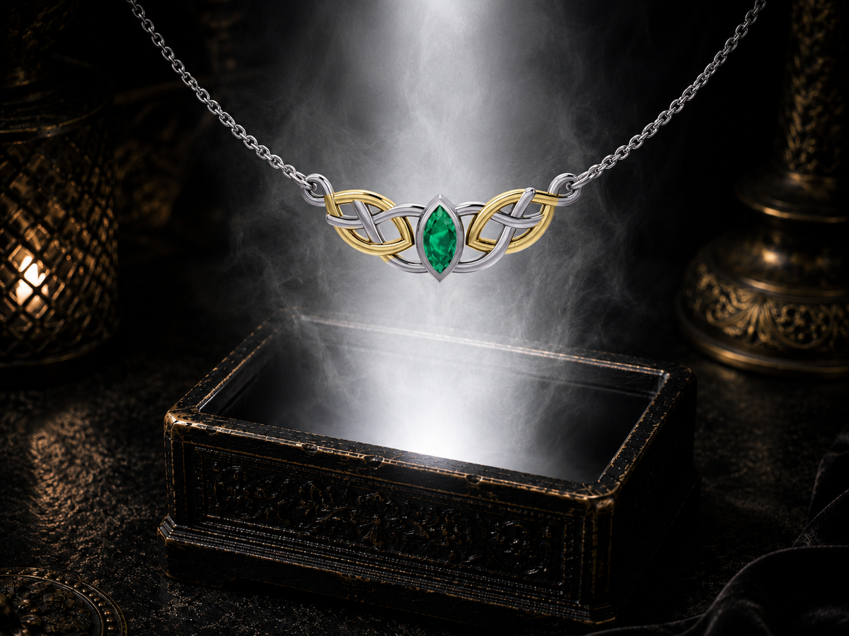Sterling silver Celtic knotwork necklace with 14K gold accents and emerald glass gemstone floating above an ornate dark jewelry box illuminated by warm radiant light.