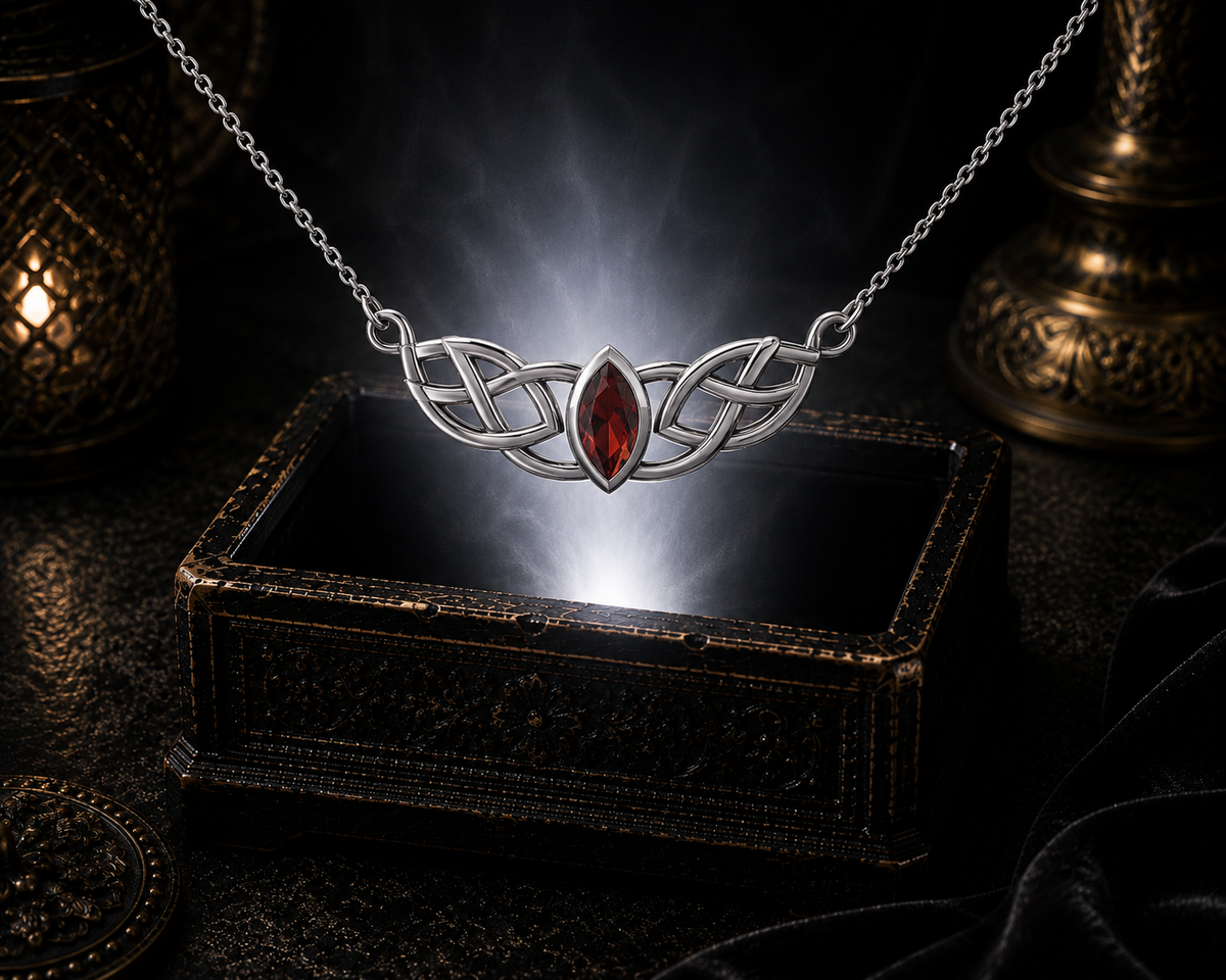 Sterling silver Celtic knotwork pendant with garnet gemstone displayed above an ornate dark jewelry box against a shadowed luxury backdrop
