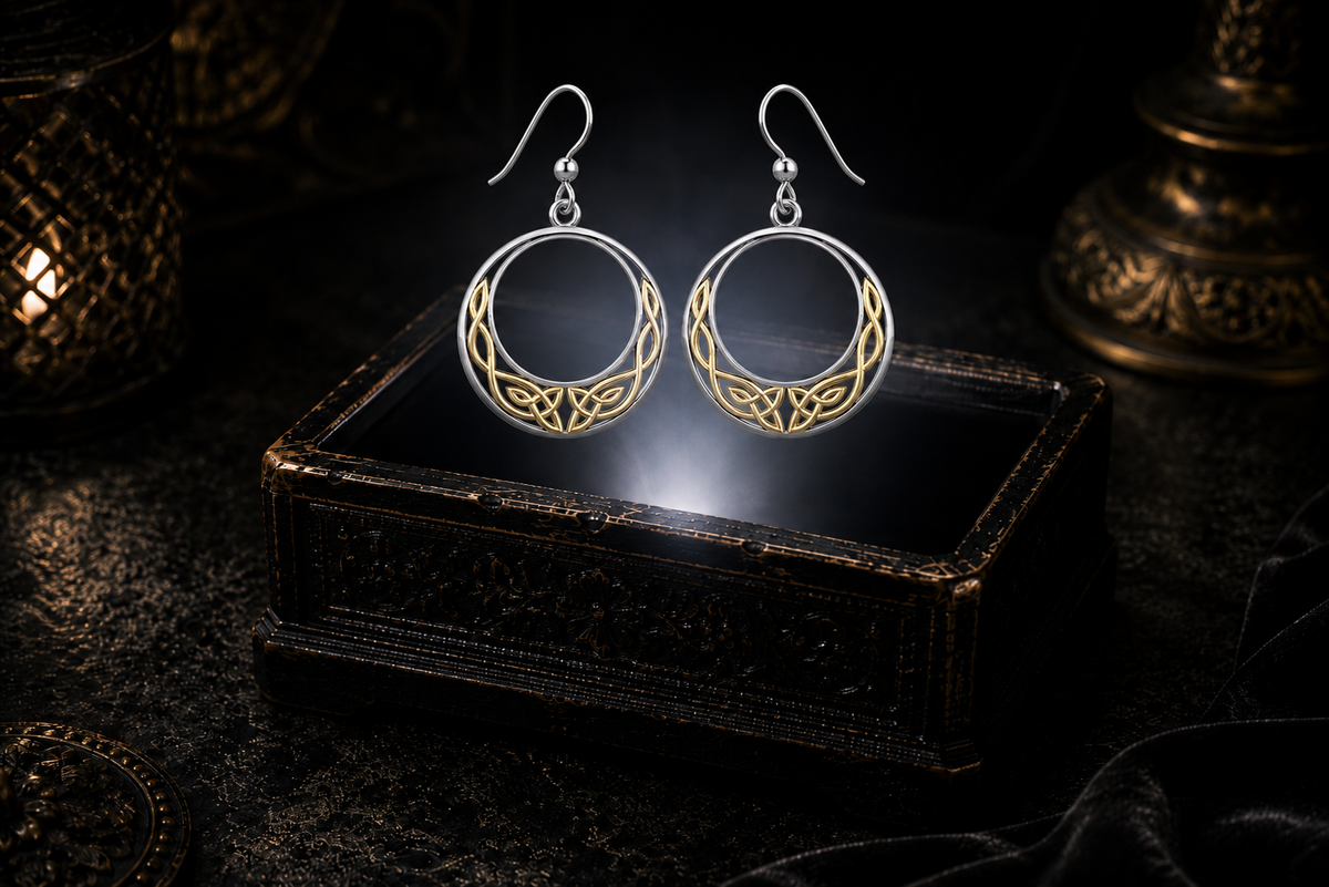 Sterling silver Celtic moon earrings with 14K gold knotwork accents floating above a glowing ornate jewelry box in a dark luxury setting