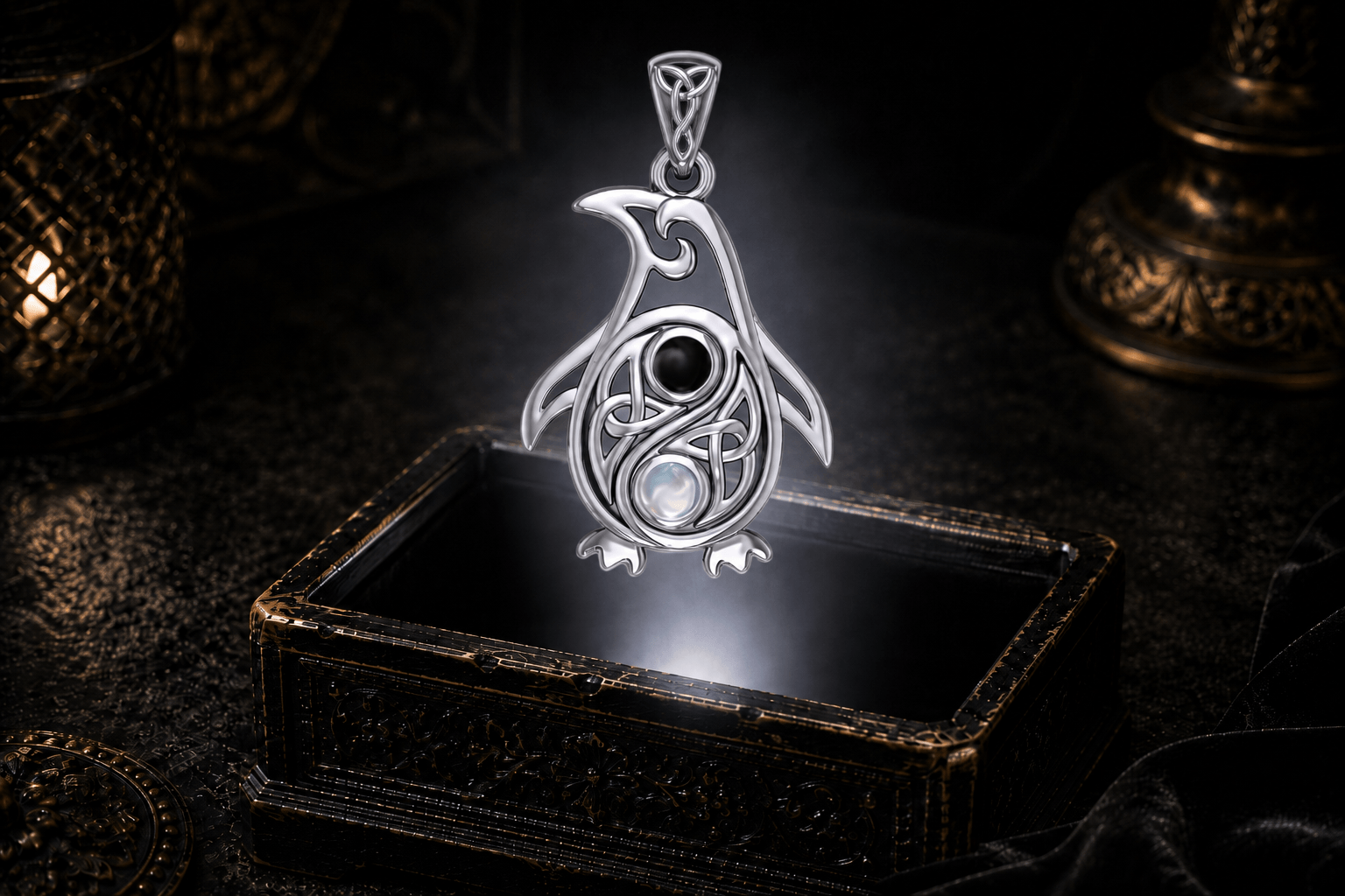 Celtic penguin pendant with black onyx and rainbow moonstone hovering above an ornate antique jewelry box in a white light beam