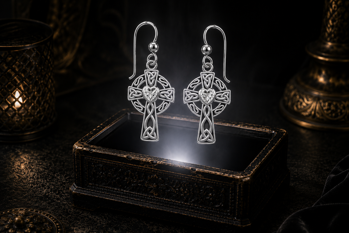Sterling silver Celtic ringed cross earrings with cubic zirconia heart gemstones floating above a glowing ornate jewelry box in a dark luxury setting