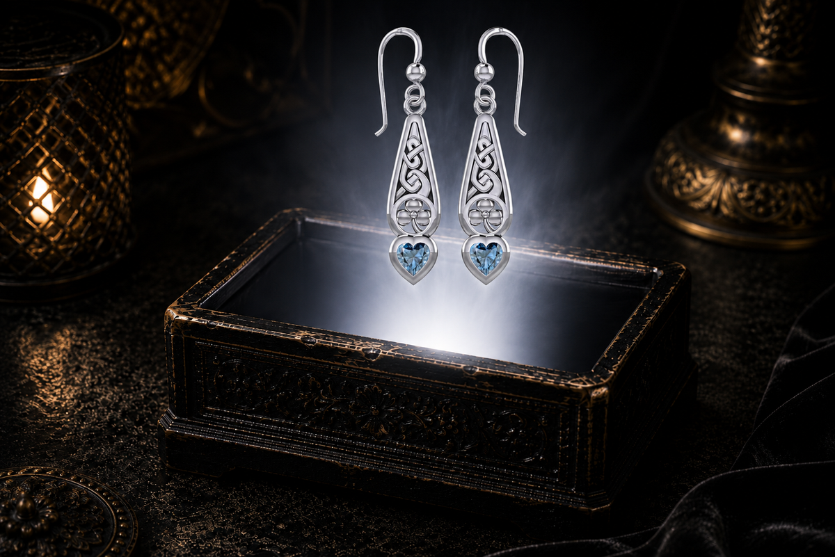 Sterling silver Irish shamrock earrings featuring heart-shaped blue topaz gemstones showcased above a luminous ornamental jewelry box in an elegant mythic luxury environment.