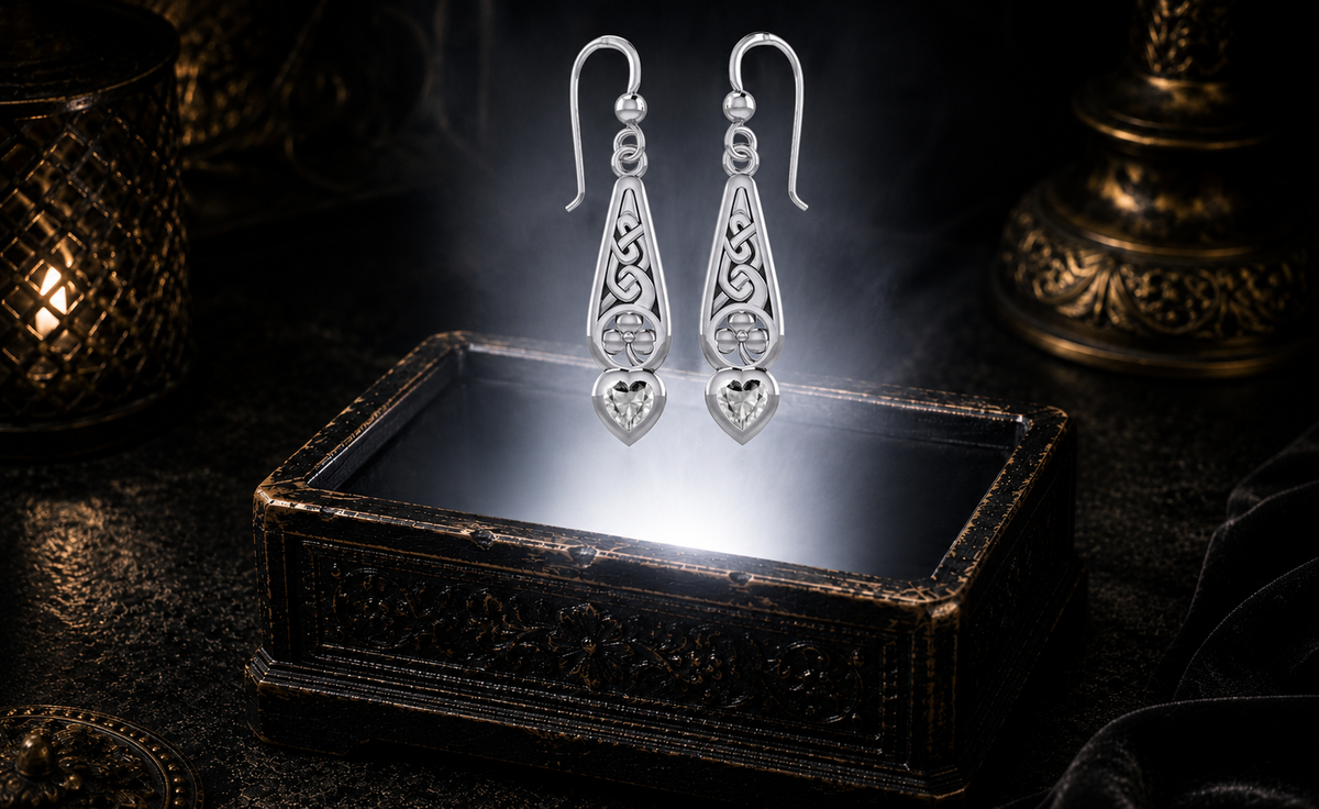 Sterling silver Celtic shamrock heart earrings with sparkling cubic zirconia gemstones displayed above an ornate jewelry chest illuminated by soft white light and cinematic atmosphere.