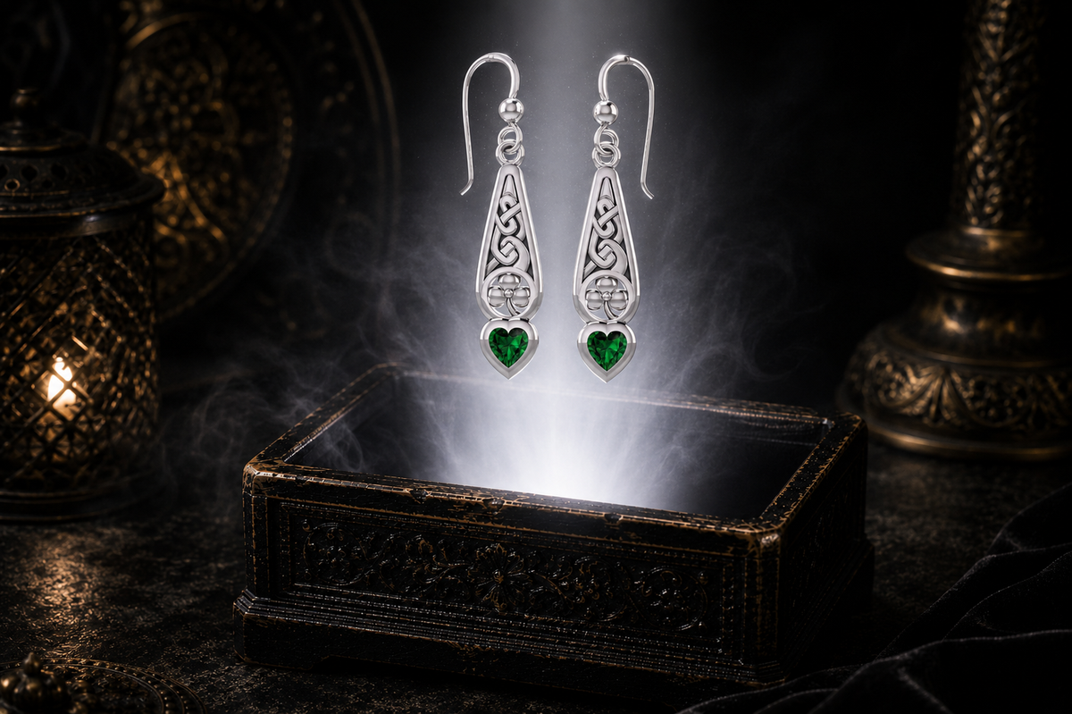 Sterling silver Celtic shamrock drop earrings with heart-shaped emerald glass gemstones floating above an ornate jewelry box in a dark luxury setting illuminated by soft glowing light.