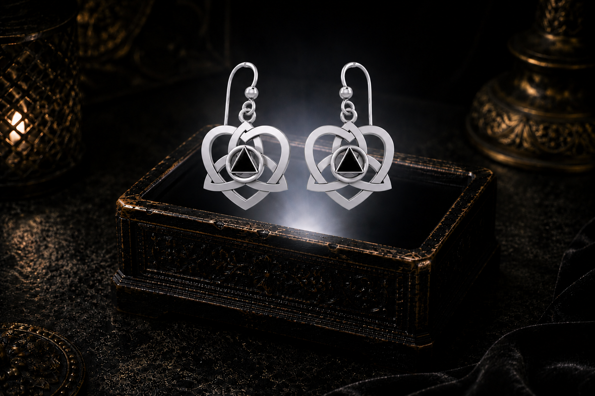 Sterling silver Celtic Trinity heart recovery earrings with black onyx triangle stones floating above a glowing ornate jewelry box in a dark luxury setting