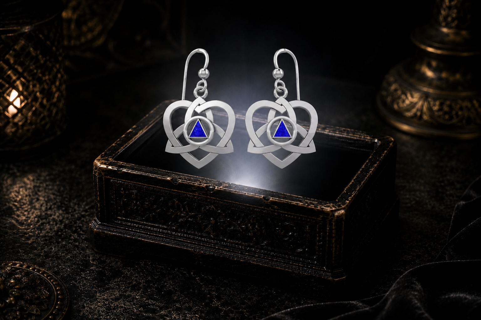 Sterling silver Celtic Trinity heart recovery earrings with lapis triangle stones floating above a glowing ornate jewelry box in a dark luxury setting