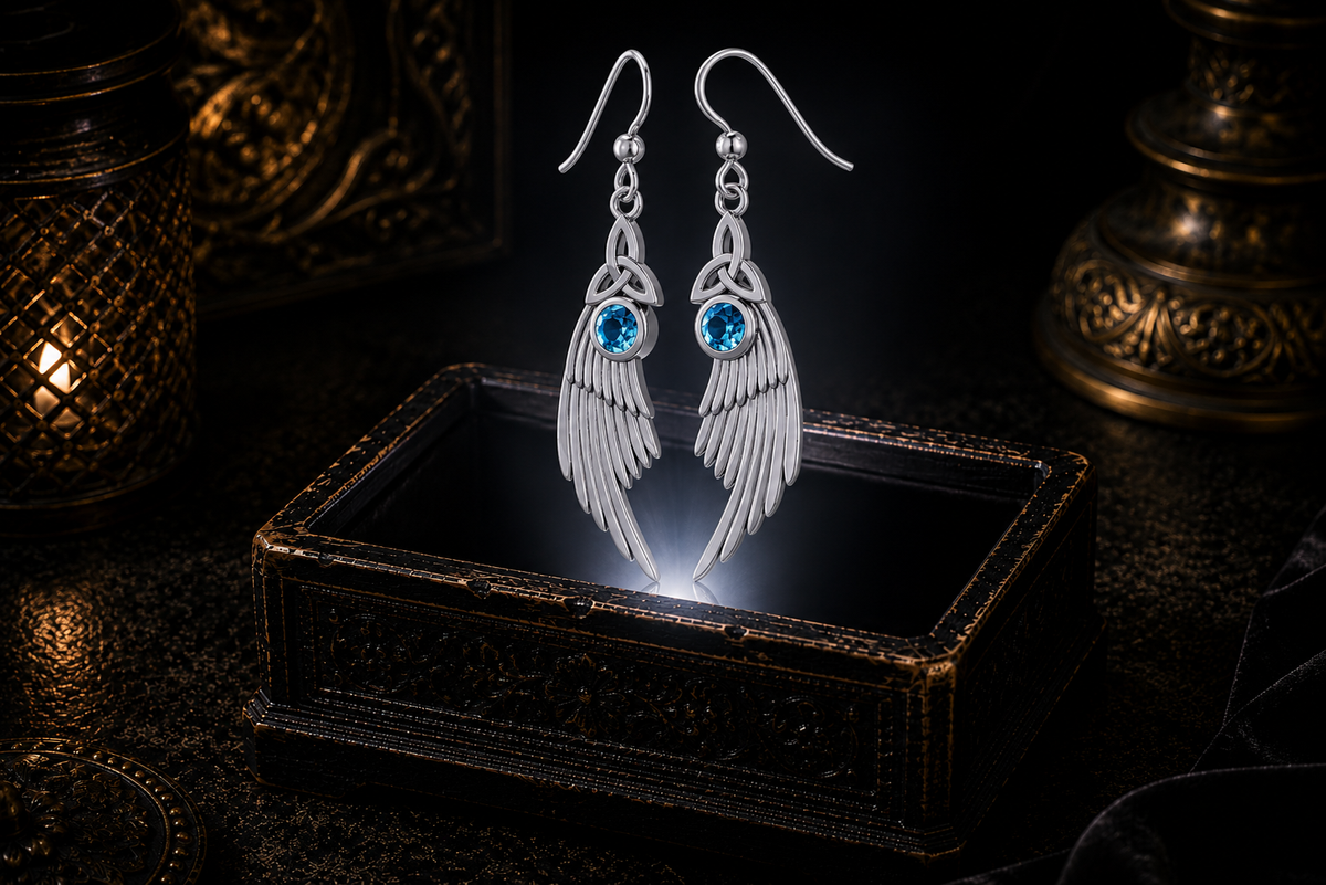 Sterling silver Celtic Trinity Knot angel wing earrings with blue topaz gemstones floating above a glowing ornate jewelry box in a dark luxurious mystical setting with cinematic lighting