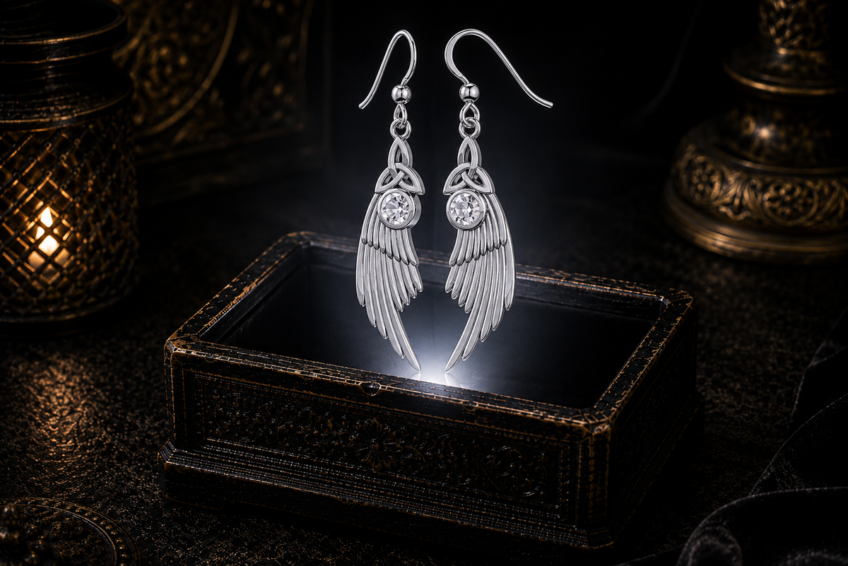 Sterling silver Celtic Trinity Knot angel wing earrings with cubic zirconia gemstones floating above a glowing ornate jewelry box in a dark luxurious mystical setting with cinematic lighting