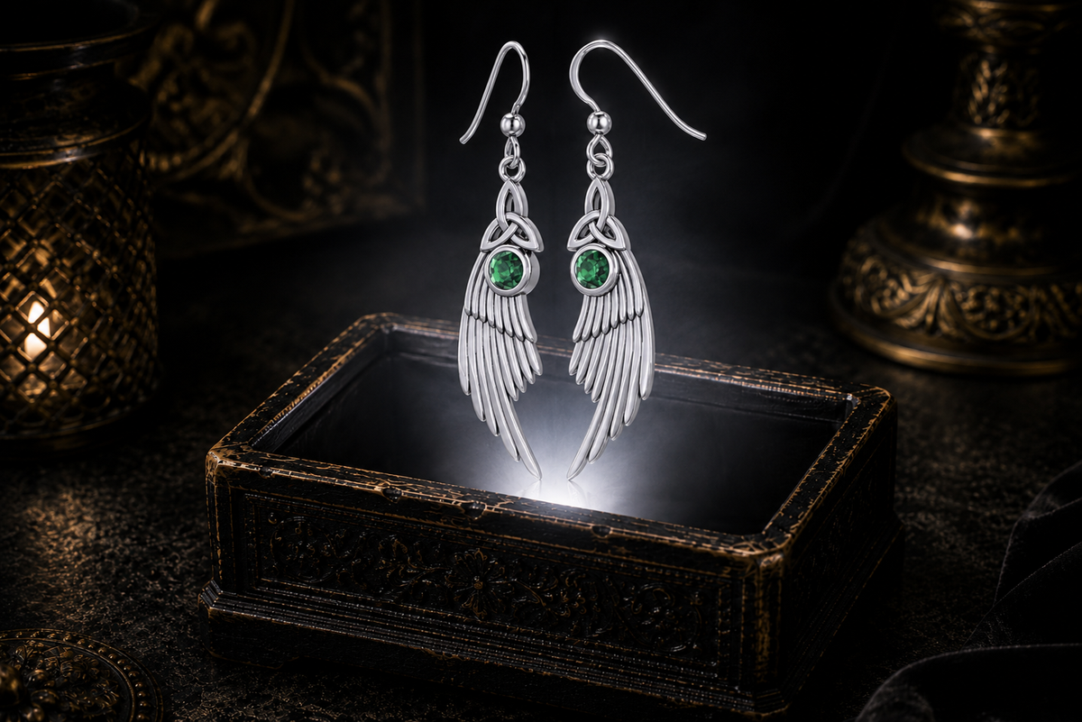 Sterling silver Celtic Trinity Knot angel wing earrings with emerald green gemstones floating above a glowing ornate jewelry box in a dark luxurious mystical setting with cinematic lighting