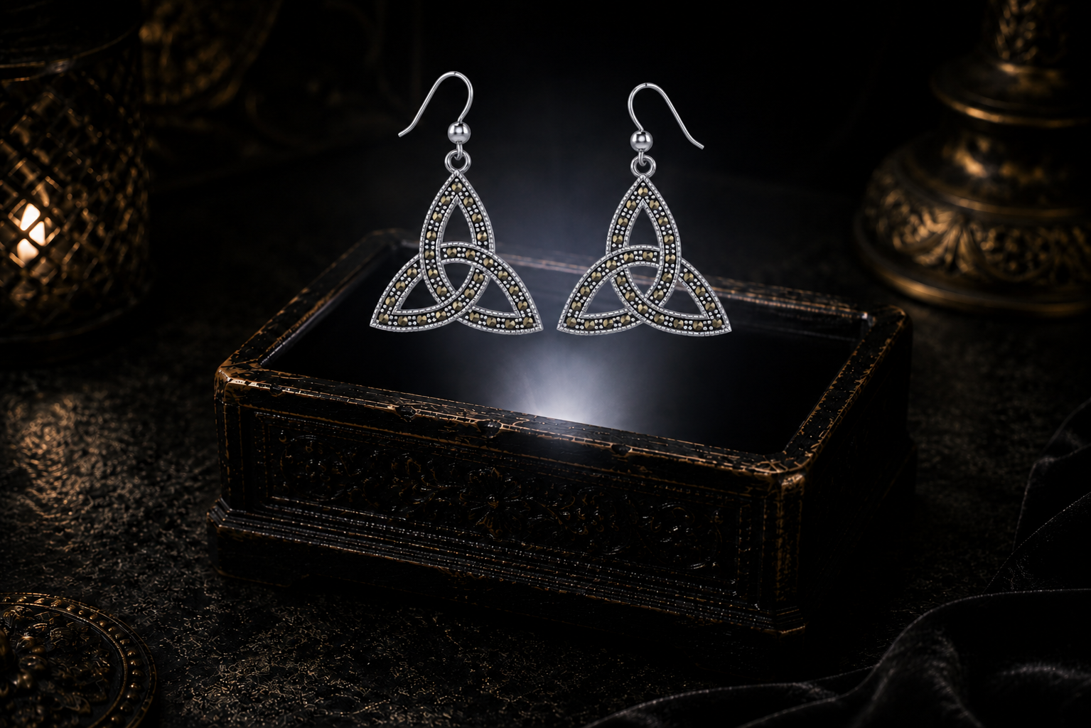 Sterling silver Celtic Trinity knot earrings lined with marcasite floating above a glowing ornate jewelry box in a dark luxury setting