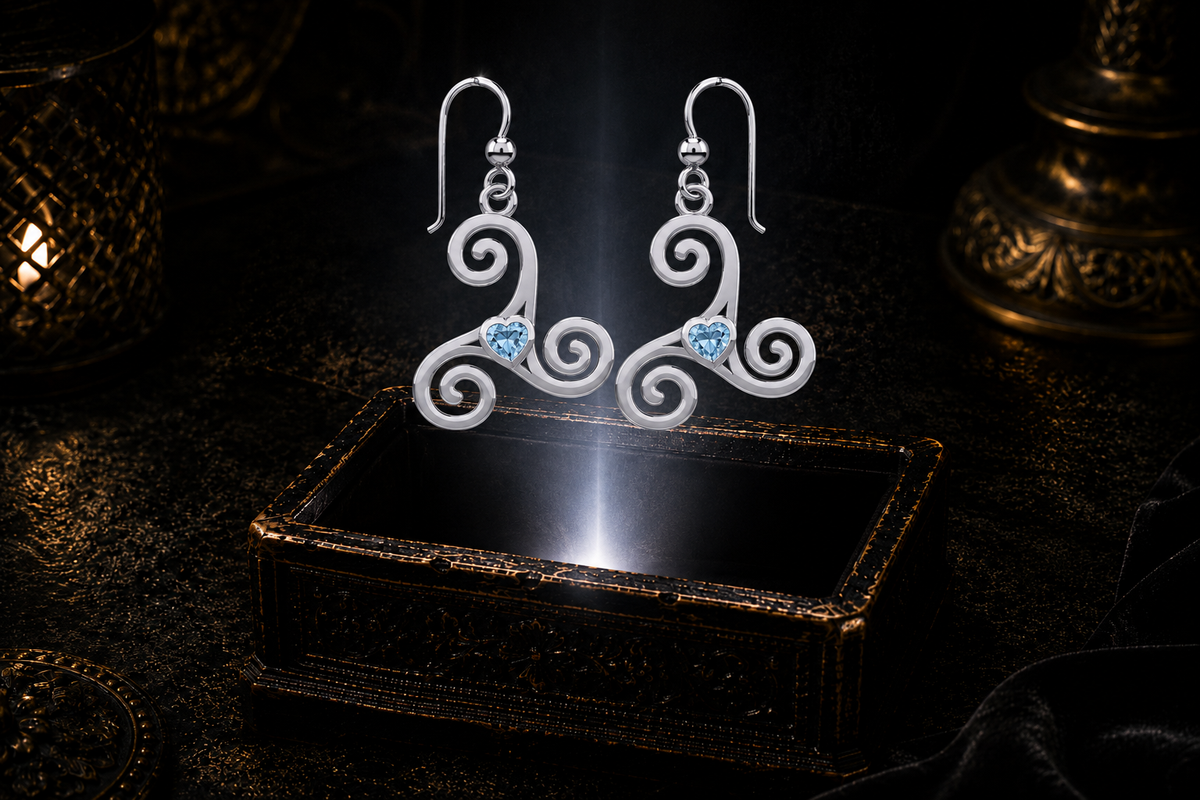 Sterling silver Celtic triskele spiral earrings with blue topaz heart gemstones floating above a glowing ornate jewelry box in a dark luxury setting