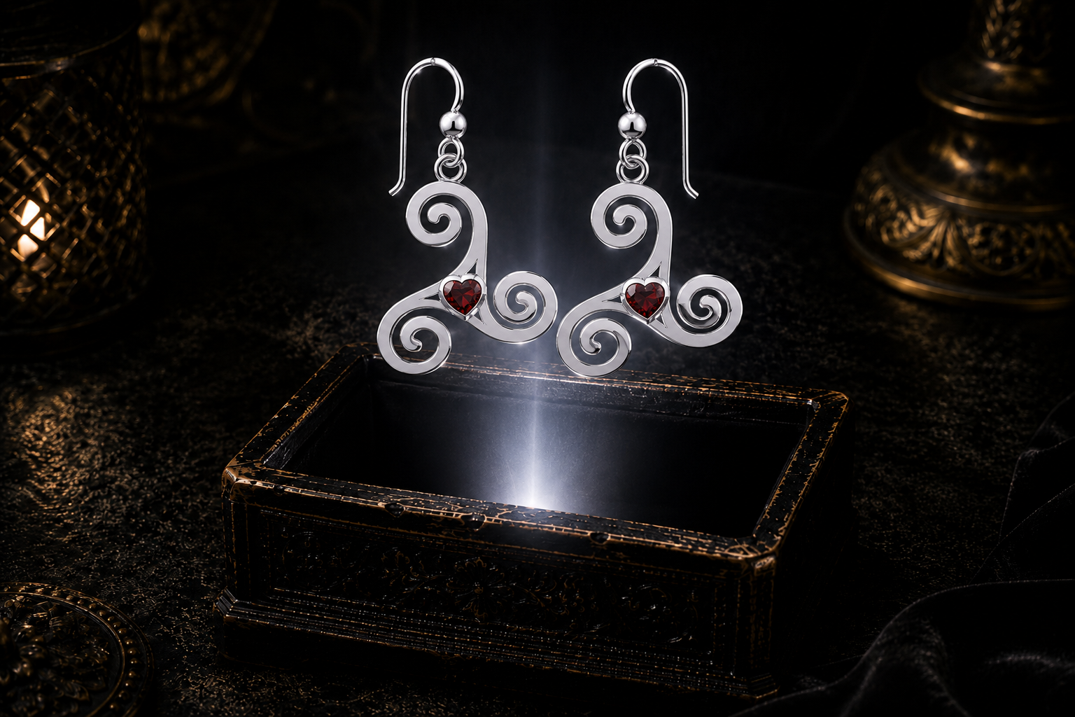 Sterling silver Celtic triskele spiral earrings with garnet heart gemstones floating above a glowing ornate jewelry box in a dark luxury setting