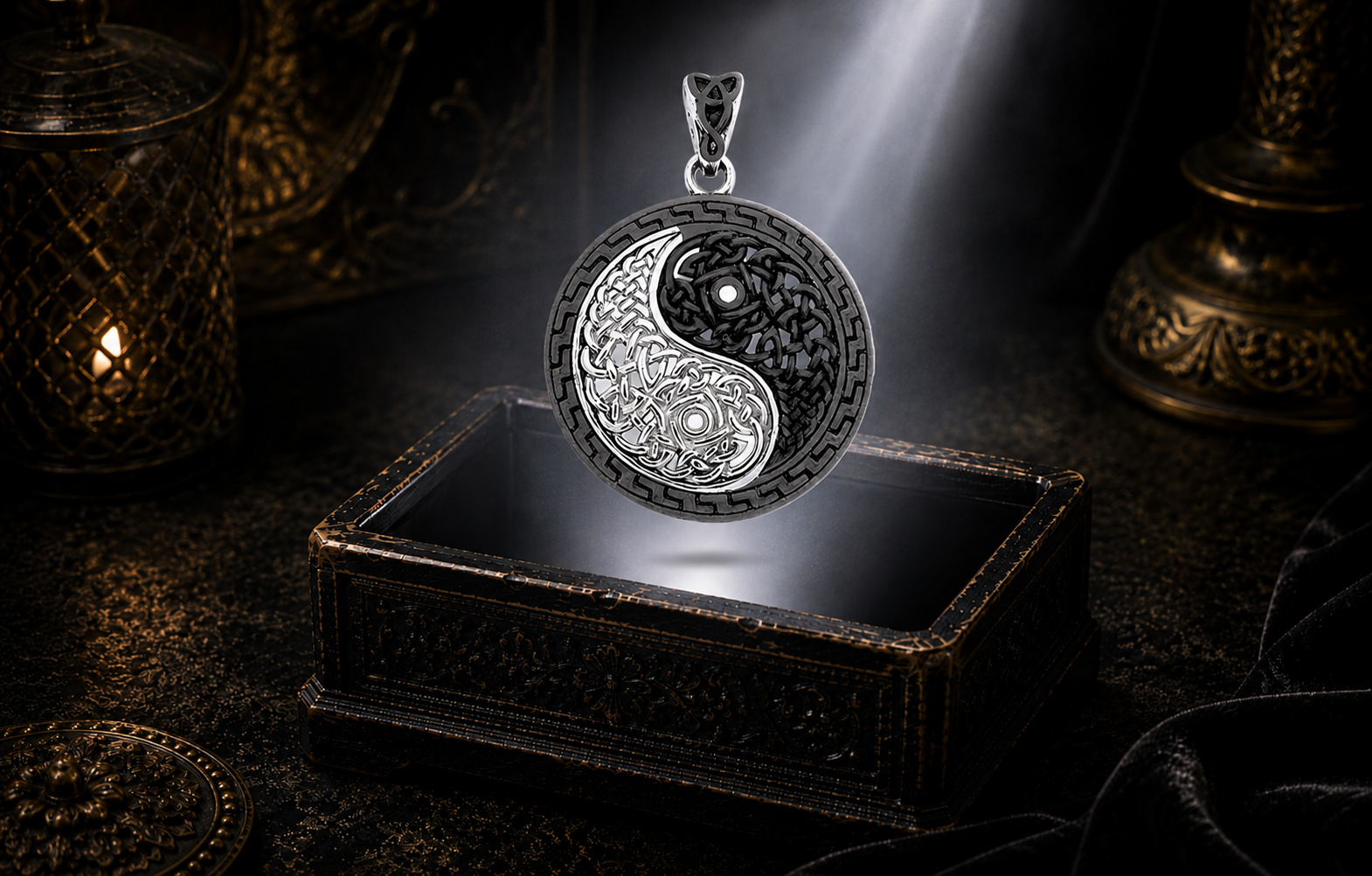 Sterling silver Celtic Yin Yang pendant with black rhodium accents and intricate Celtic knotwork floating above an ornate jewelry box beneath a radiant beam of light in a dark luxury setting.
