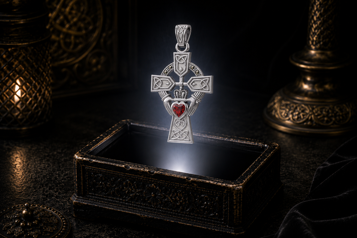 14K white gold Claddagh Celtic Cross pendant with a heart-shaped faceted garnet, flowing Celtic knotwork, and marcasite accent stones floating above an ornate jewelry box in a refined dark luxury setting with warm candlelight, cinematic lighting, and a mystical atmosphere.