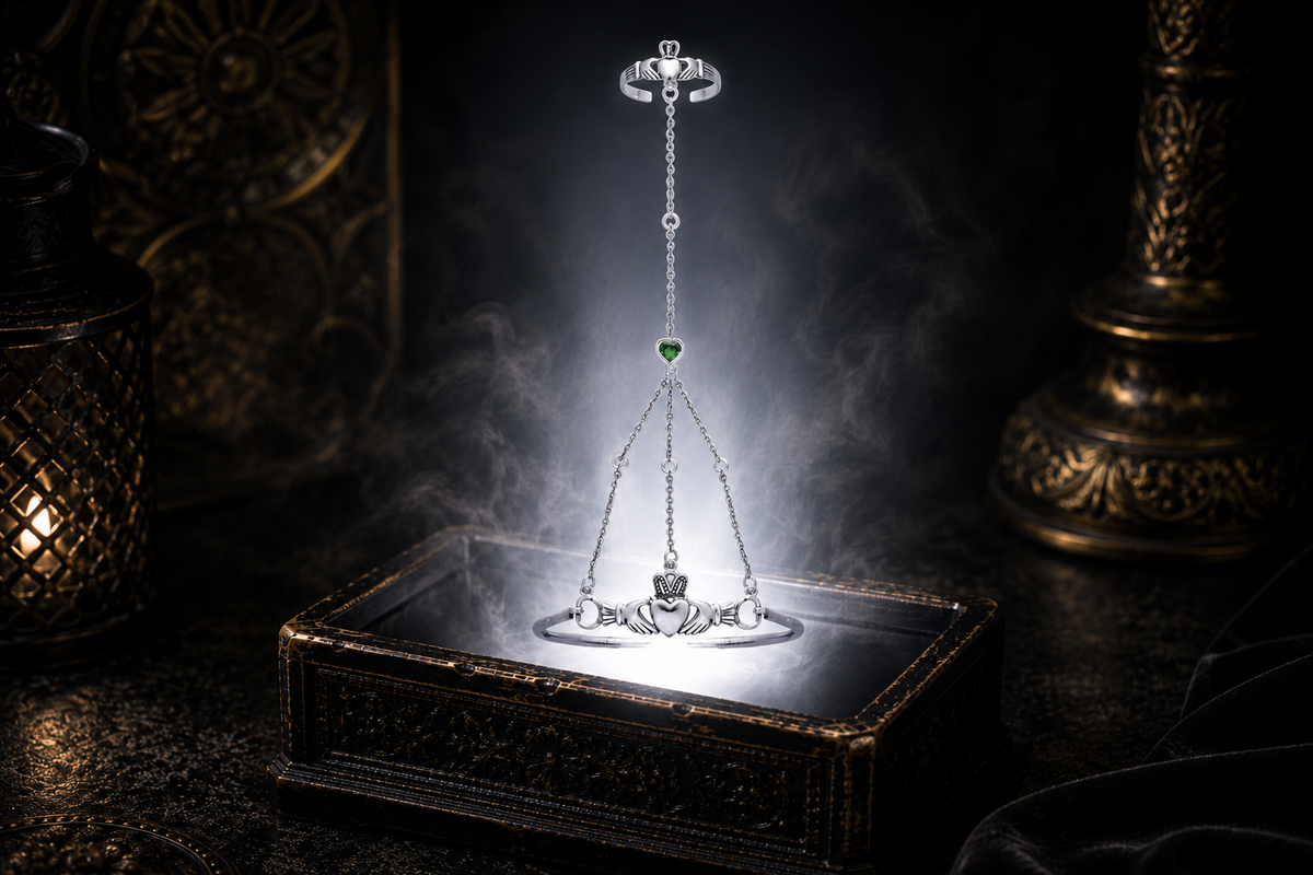 Sterling silver Claddagh hand chain bracelet with matching finger ring and emerald glass heart gemstone floating above an ornate jewelry box illuminated by soft white light in a dark luxury setting inspired by Irish heritage and timeless elegance.