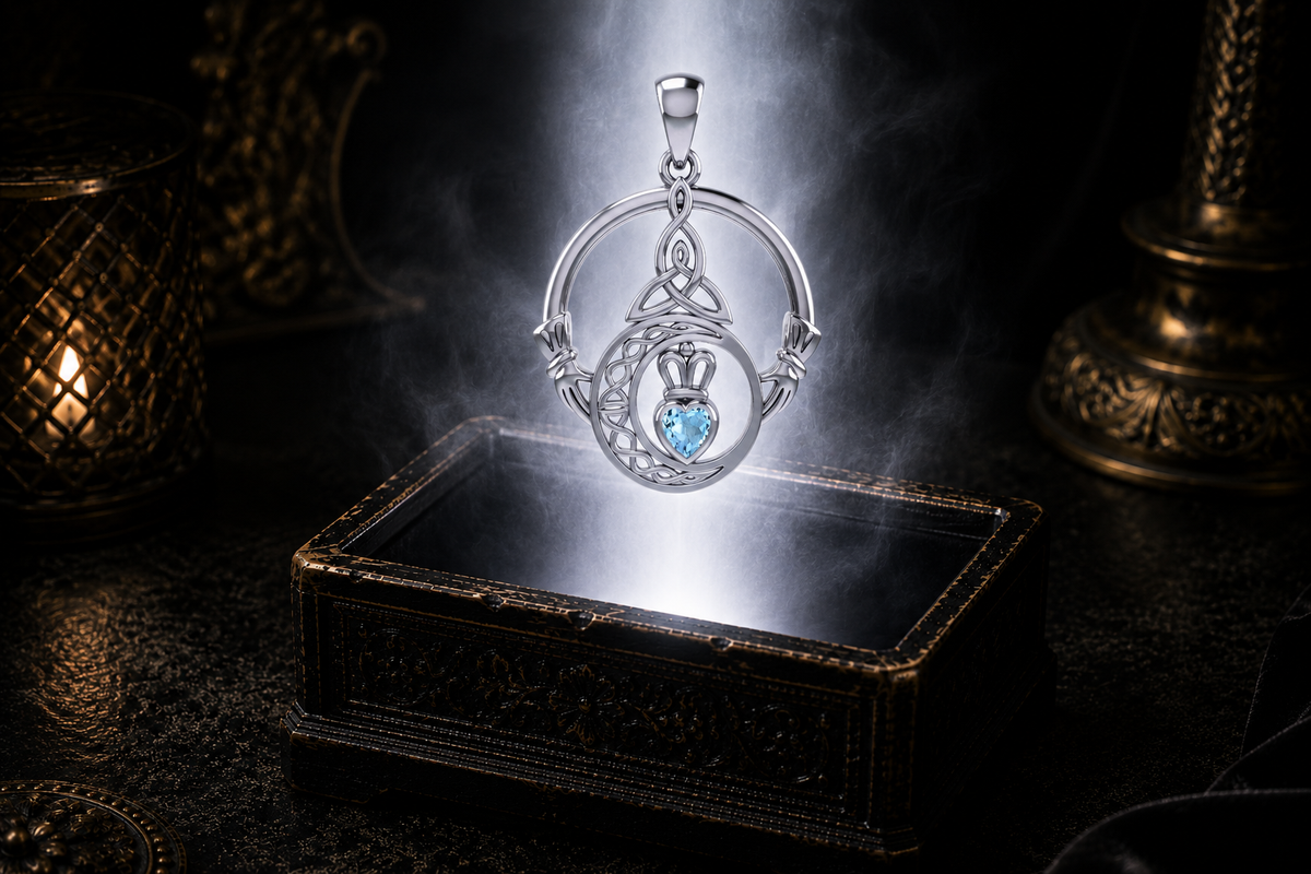 Sterling silver Claddagh Trinity Moon pendant with blue topaz gemstone displayed above a luminous jewelry chest in a cinematic shadowed setting, featuring Celtic knotwork, a crescent moon, and a crowned heart.