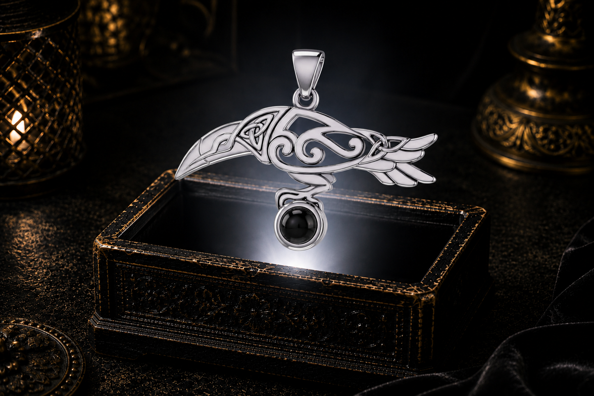 Sterling silver Celtic raven pendant with black onyx cabochon gemstone displayed above an ornate jewelry box surrounded by rich shadows in a refined luxury environment.