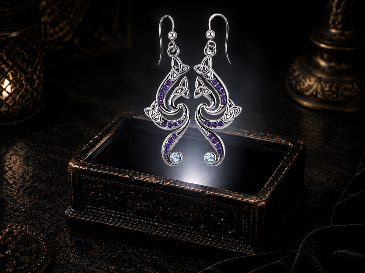 Sterling silver flowing Celtic Triquetra dangle earrings with amethyst and blue topaz gemstones floating above a glowing ornate jewelry box in a dark luxury setting