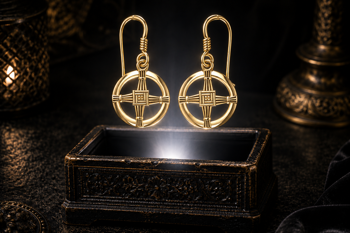 St. Brigid's Cross dangle earrings in solid yellow gold with round open frames, woven cross centers, and curved hook ear wires - hovering above an ornate black jewelry box in a neutral white beam of light.