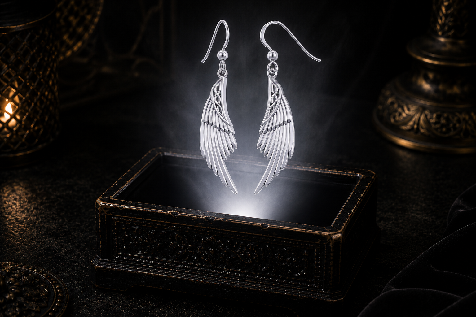 Sterling silver guardian angel wings earrings with Celtic knotwork floating above a glowing ornate jewelry box in a dark luxury setting