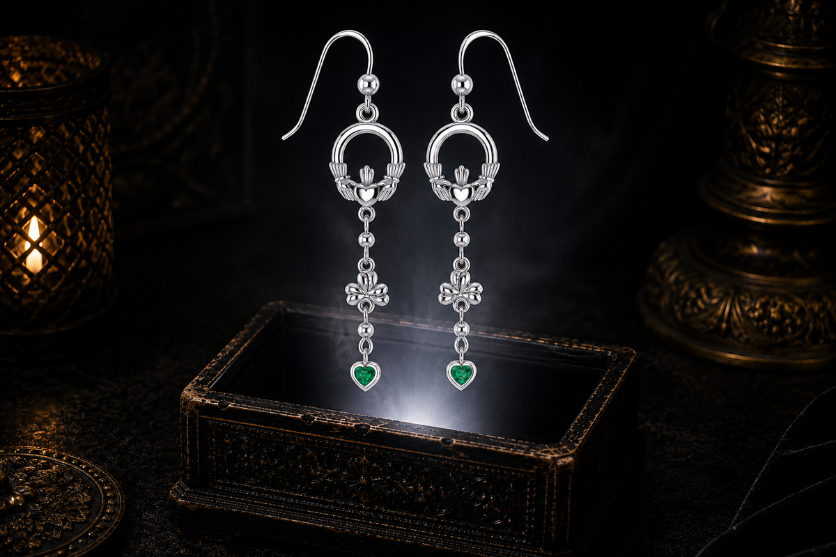 Sterling silver Irish Claddagh drop earrings with emerald heart accents floating above a glowing ornate jewelry box in a dark luxury setting