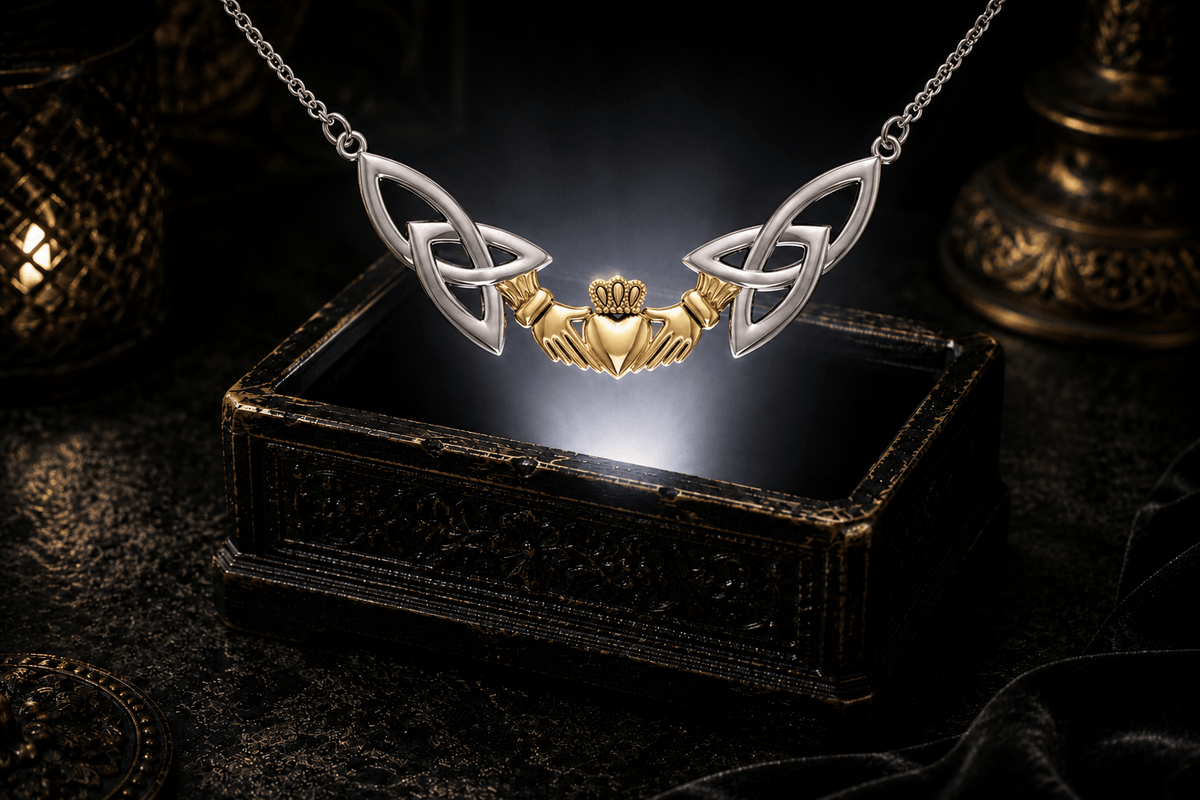 Sterling silver Irish Claddagh necklace with a 14K gold vermeil heart and Celtic Trinity Knots floating above an antique jewelry box in a cinematic luxury setting.