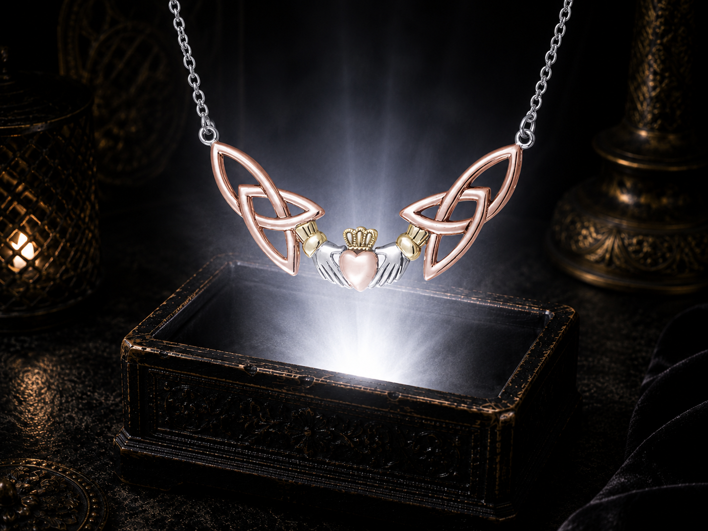 Sterling silver Irish Claddagh Trinity Knot necklace with rose gold and 14K gold accents illuminated above an ornate dark jewelry box in a cinematic luxury setting