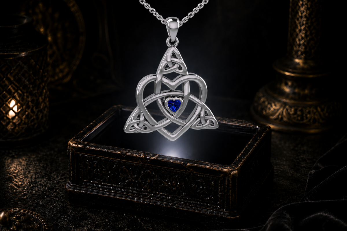 Sterling silver Celtic Trinity heart pendant with sapphire and cable chain suspended above an antique jewelry box against a dark luxury backdrop